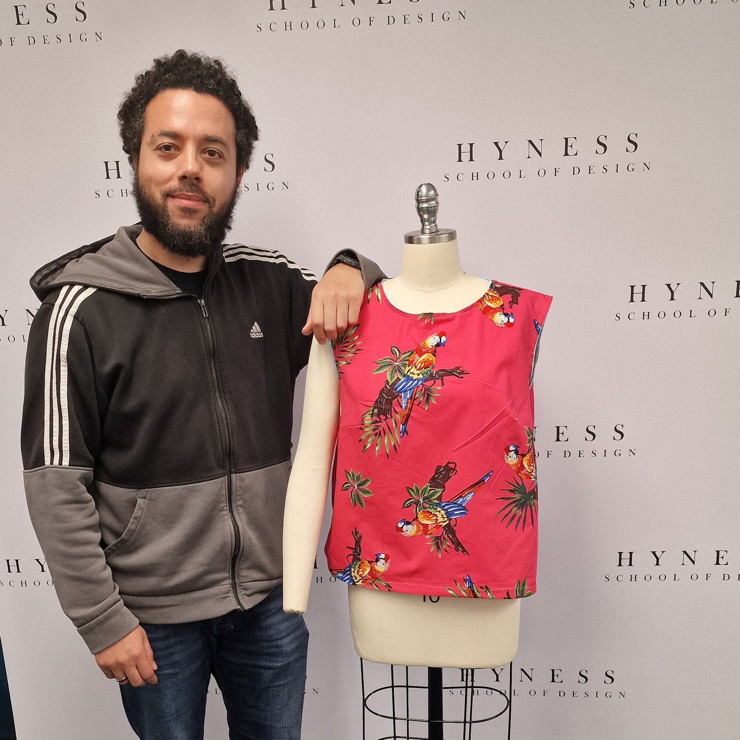 Person standing next to a mannequin wearing a red floral dress in front of a Hyness branded backdrop.