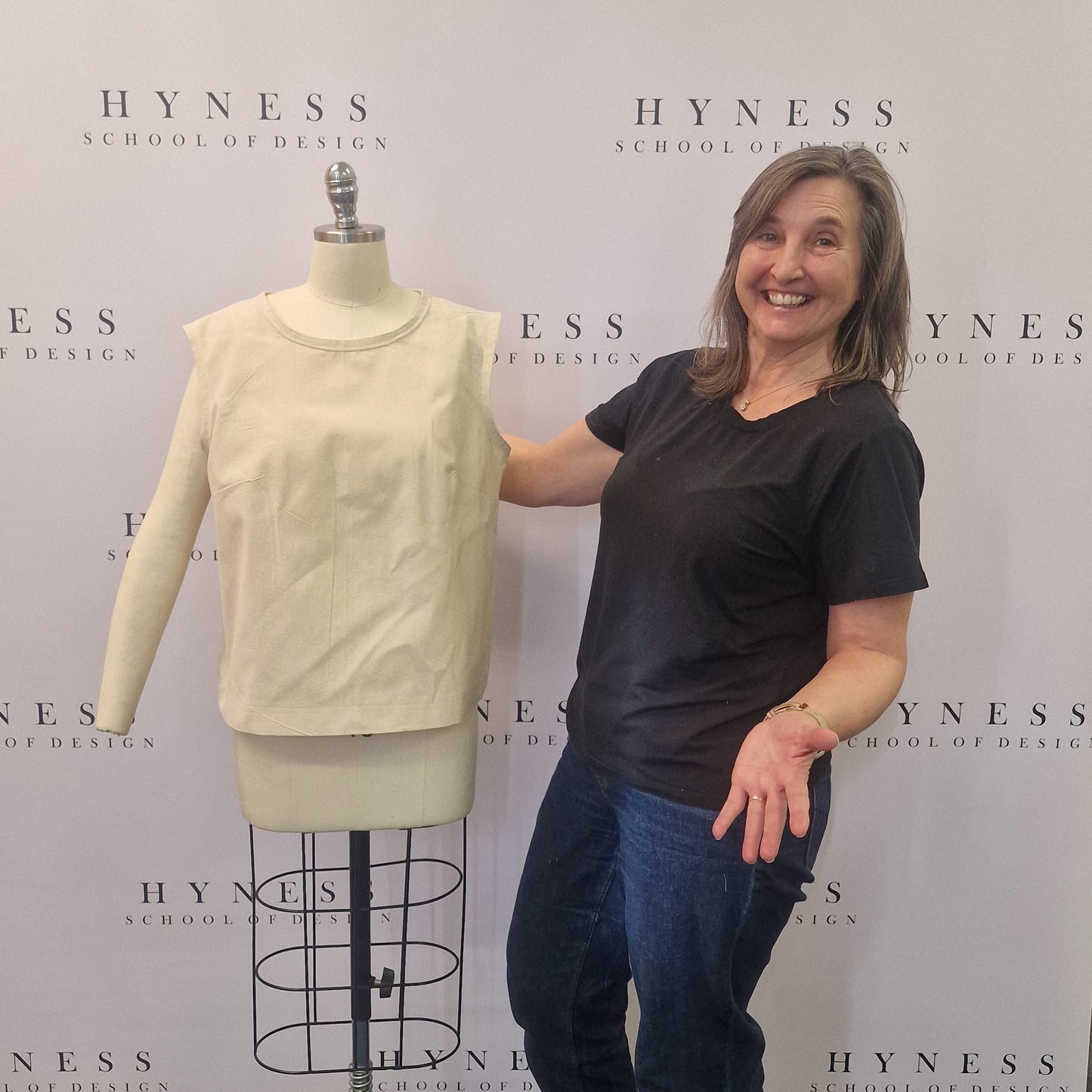 Person standing next to a mannequin wearing a dress in front of a branded backdrop