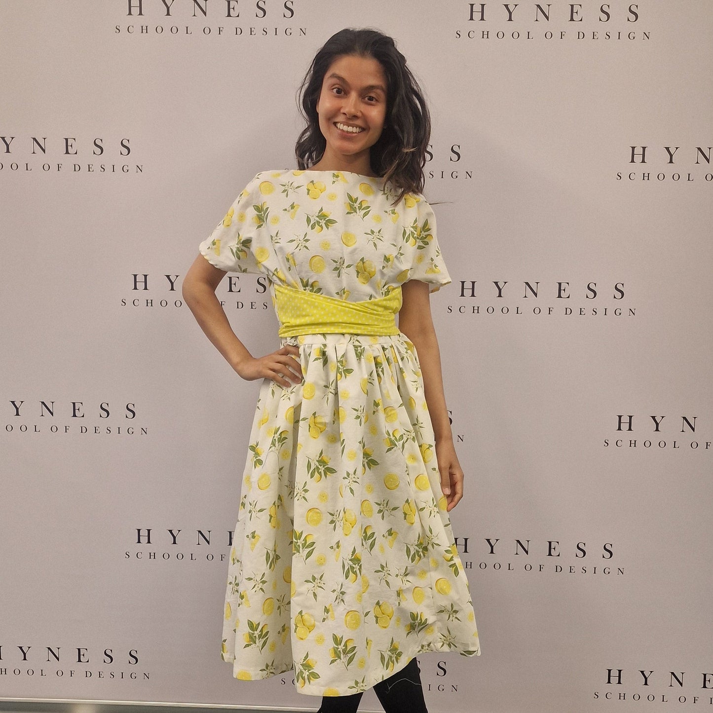 Person standing next to a large Hyness poster with a floral dress.