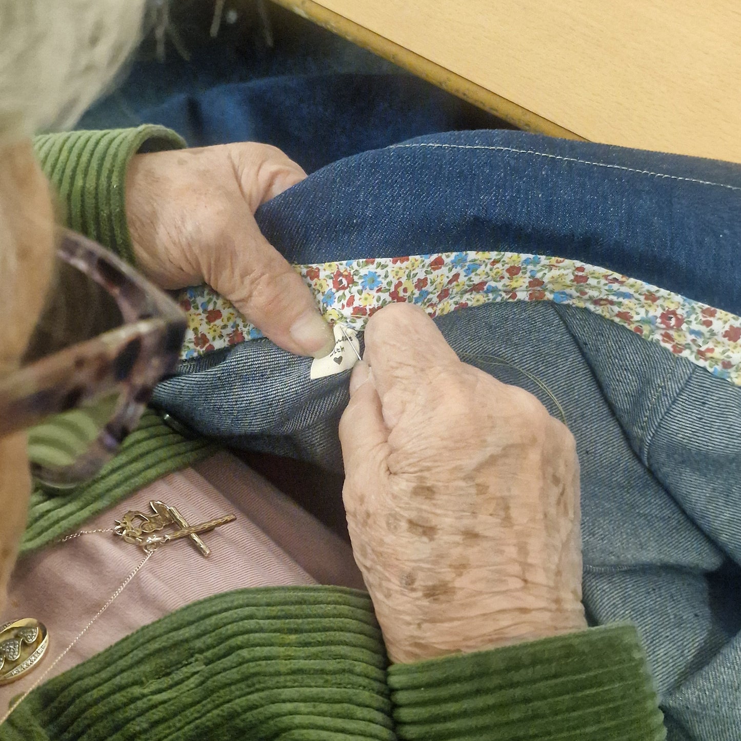 Person sewing on a piece of fabric with a needle and thread, wearing a green sweater.