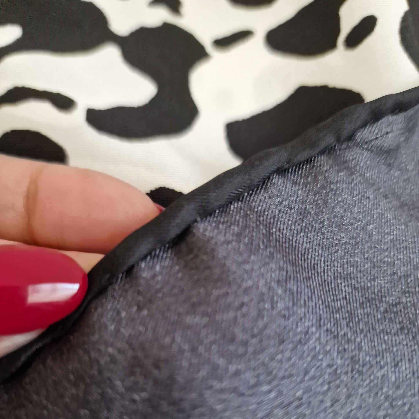 Close-up of a textured gray fabric with a hand holding it, against a patterned background.