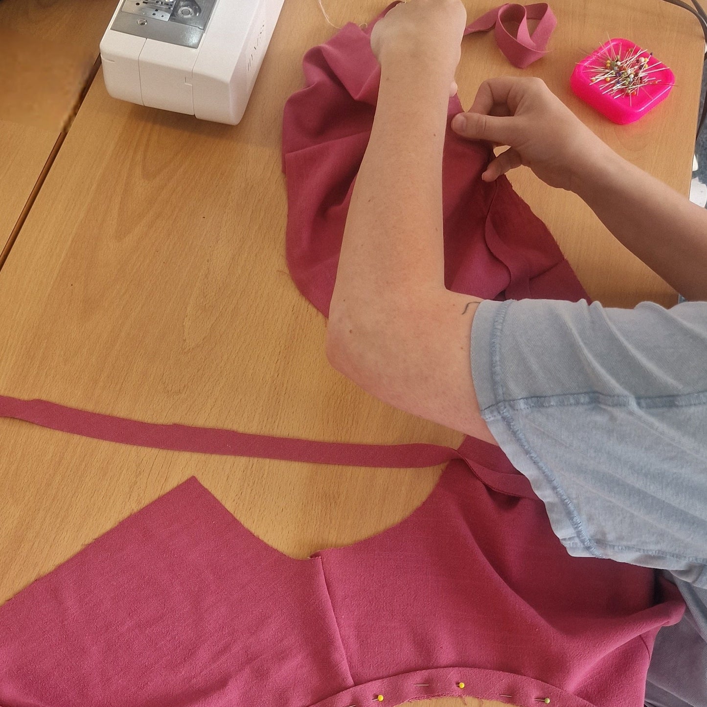 Person working on a pink garment with a sewing machine in the background