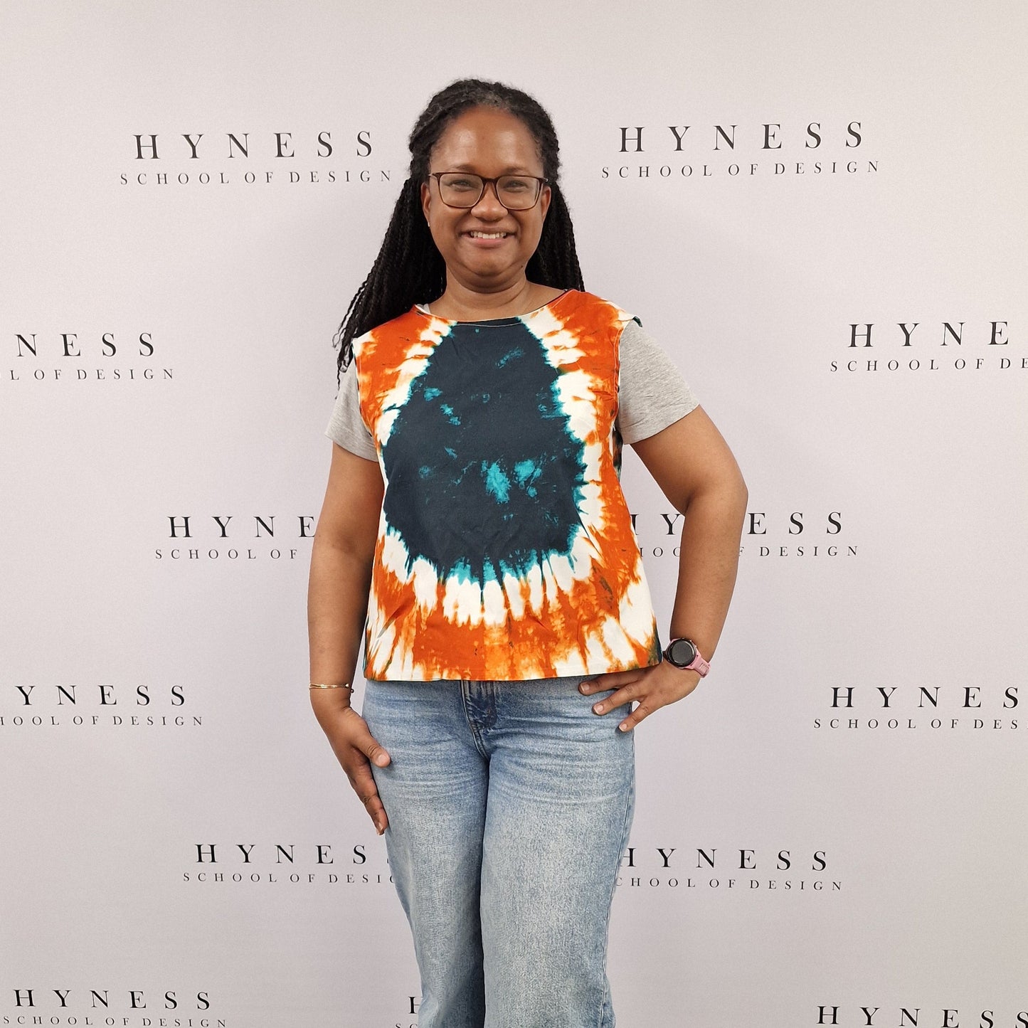 Person wearing a tie-dye shirt and jeans standing in front of a Hyness backdrop