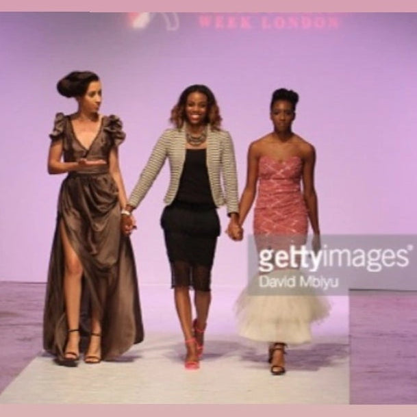 Three women walking on a runway with a pink background