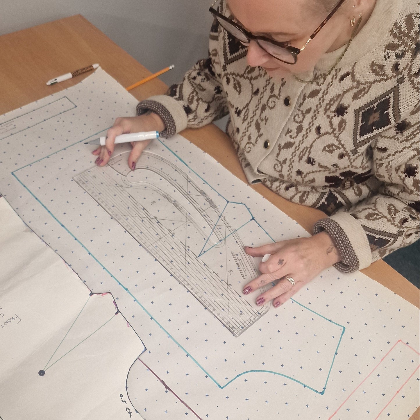 Person working on a sewing pattern with a marker on a table.