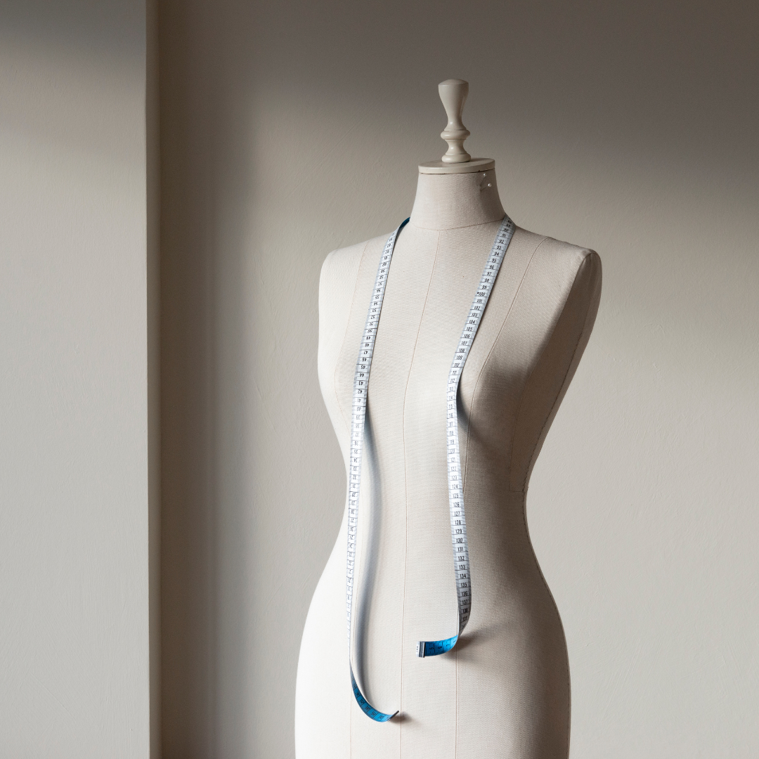 Mannequin with a measuring tape draped over it on a neutral background